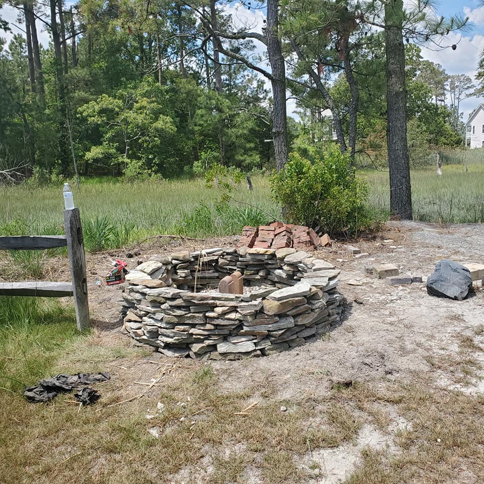 A stone fire pit is sitting in the middle of a grassy field.