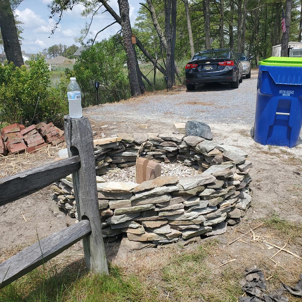 A fire pit is surrounded by rocks and a wooden fence.