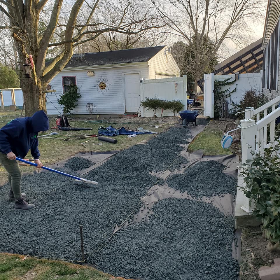 A man is raking gravel in a yard in front of a house.