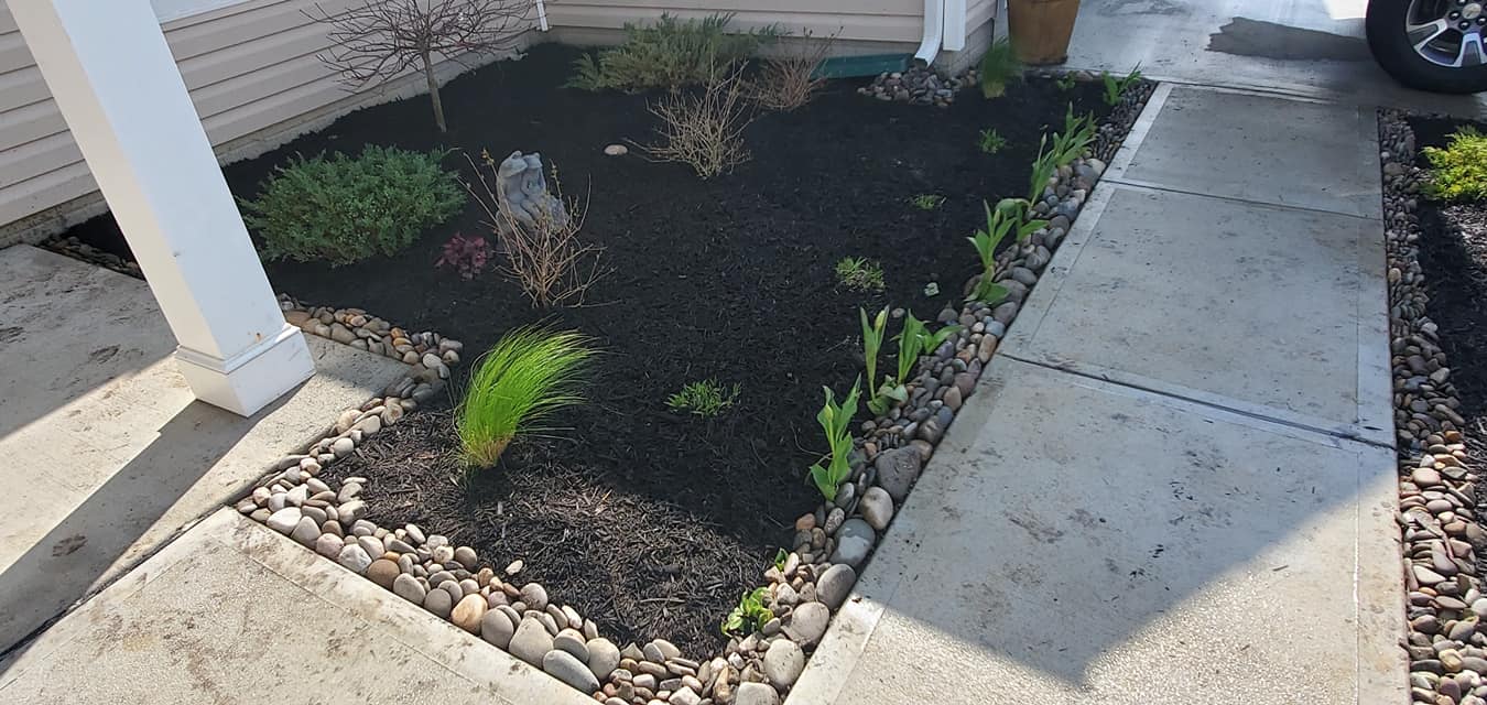 A sidewalk leading to a garden with black mulch and rocks.