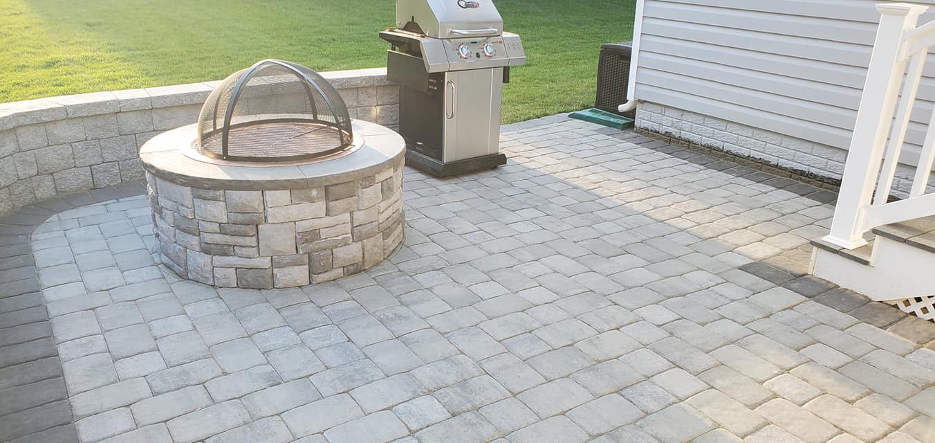A fire pit is sitting on a patio next to a grill.