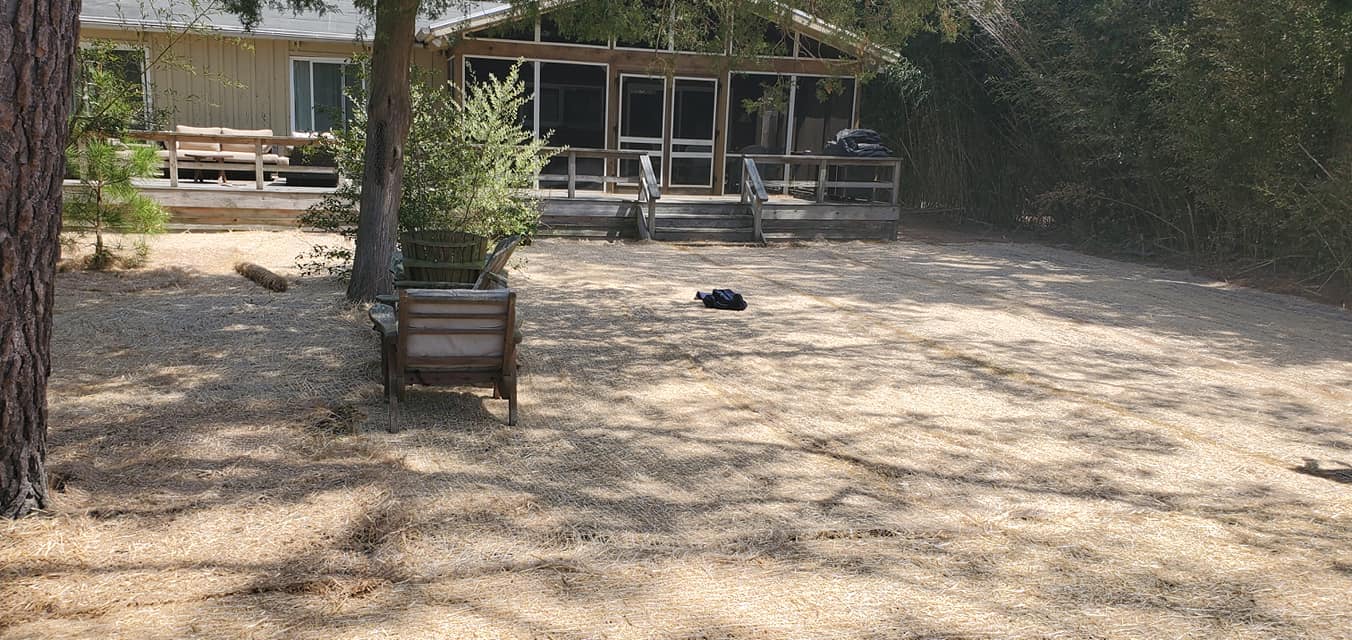 A wooden bench is sitting in the middle of a dirt field in front of a house.