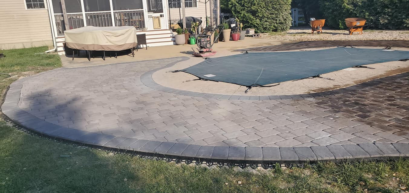 A patio with a pool in the background and a house in the background.