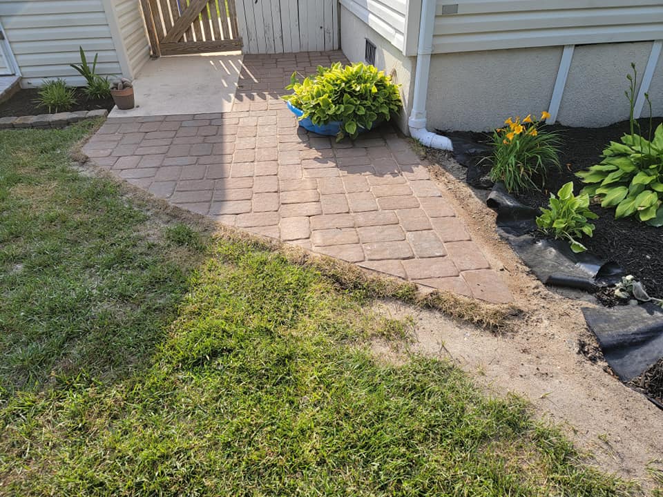 A brick walkway leading to a house with a blue potted plant on the side.