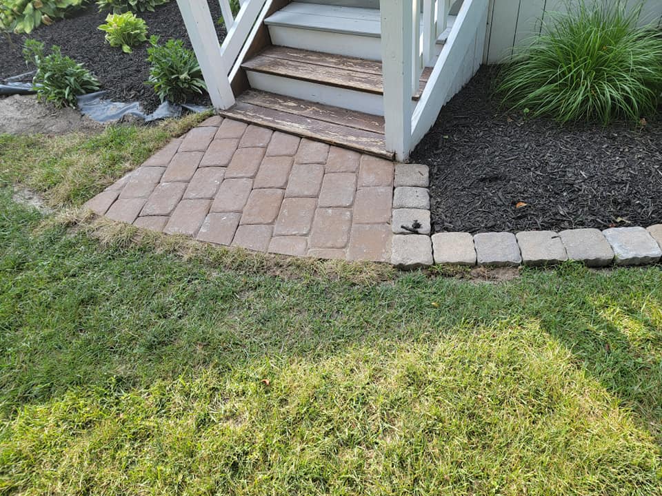 A brick walkway leading to a white house with stairs.