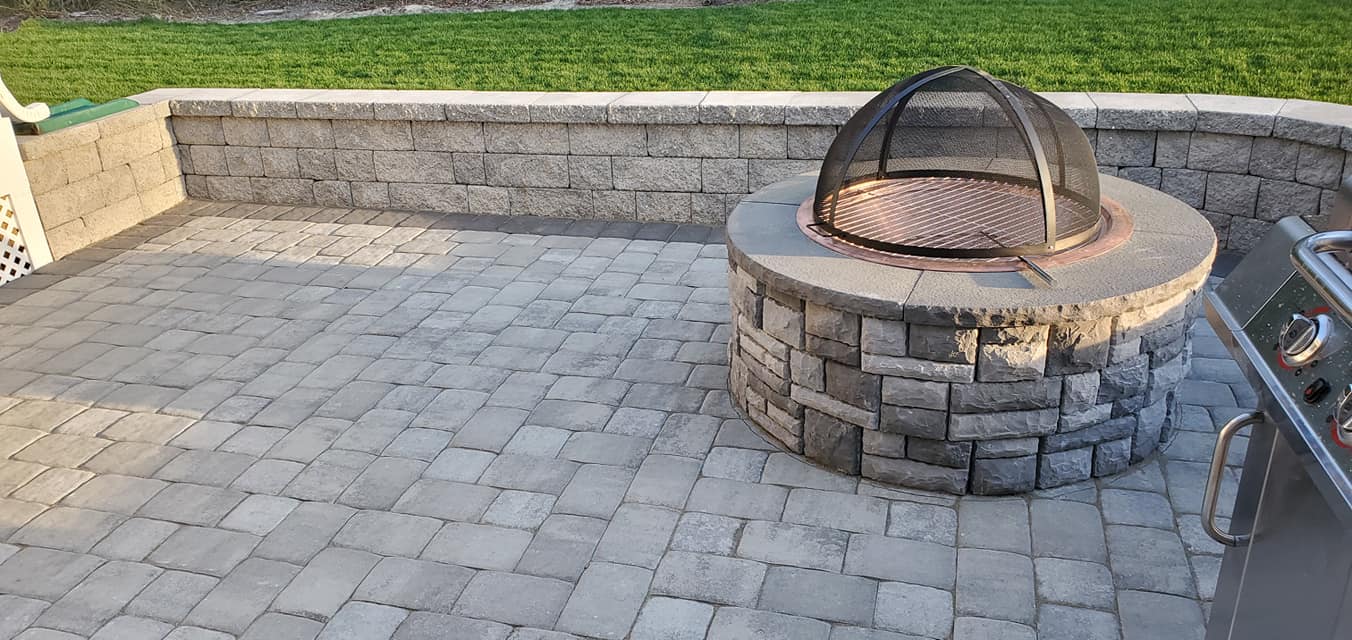 A fire pit is sitting on a patio next to a grill.