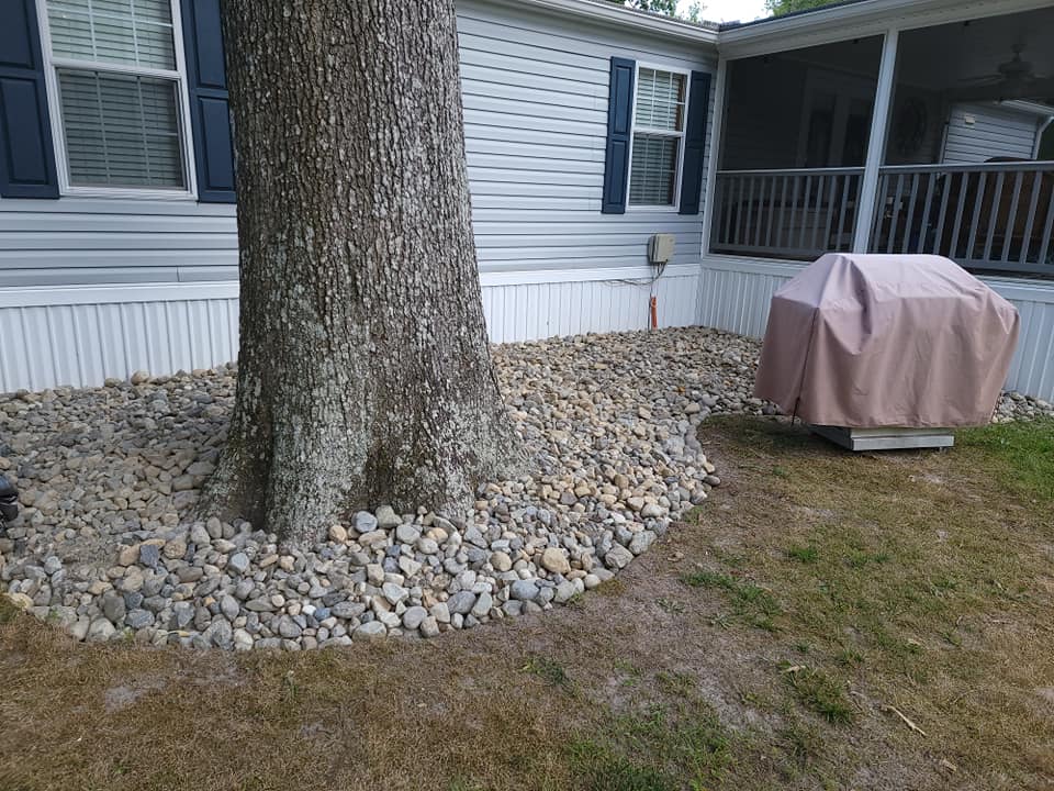 A tree is surrounded by rocks in front of a mobile home.