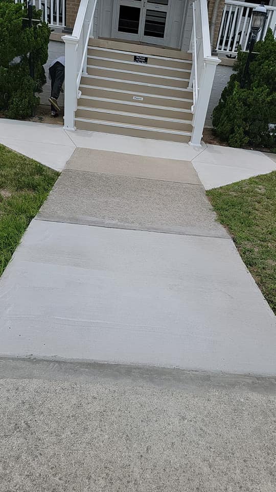 A concrete walkway leading to a house with stairs.