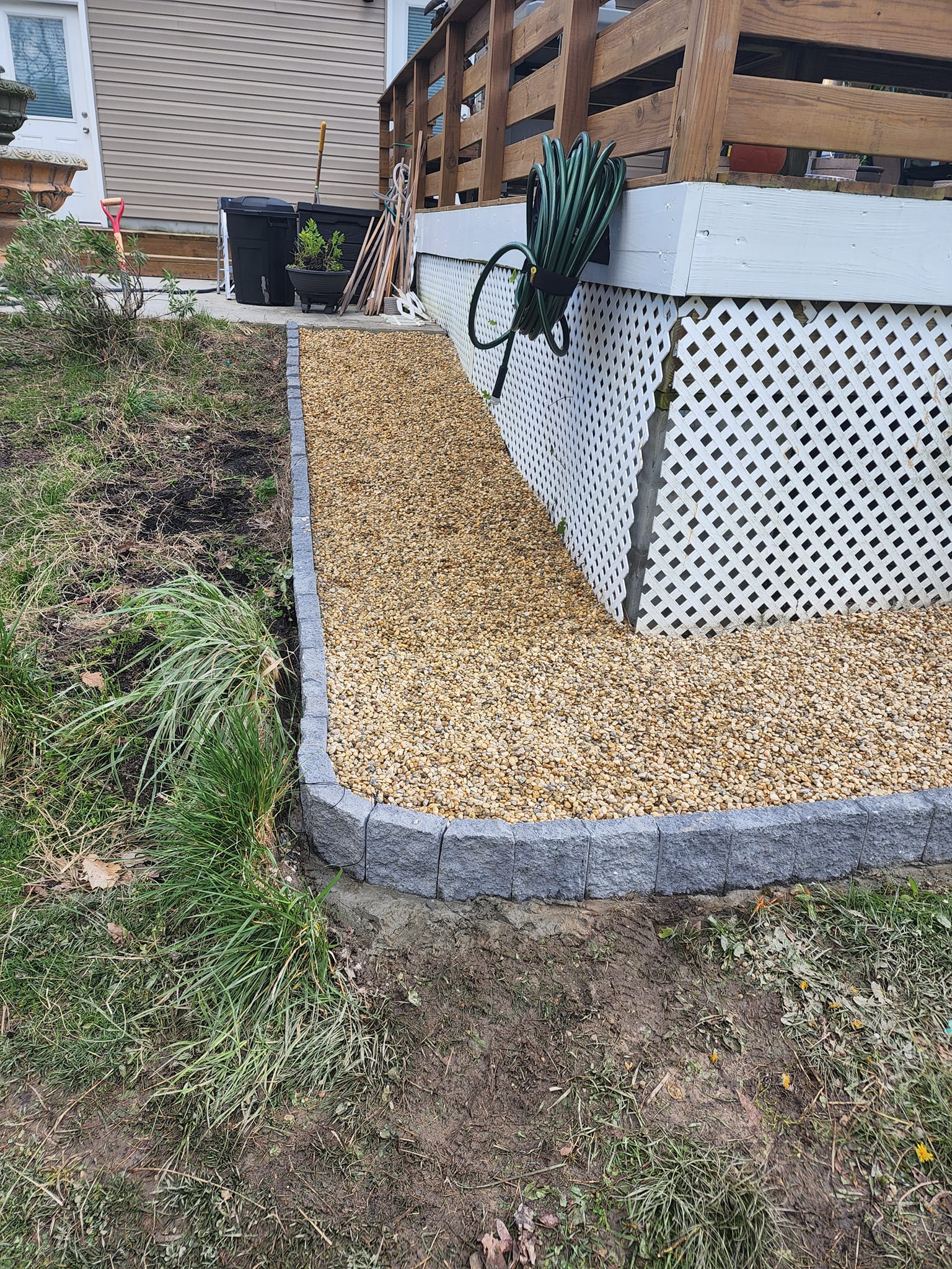 A pile of mulch is sitting on the side of a house next to a deck.