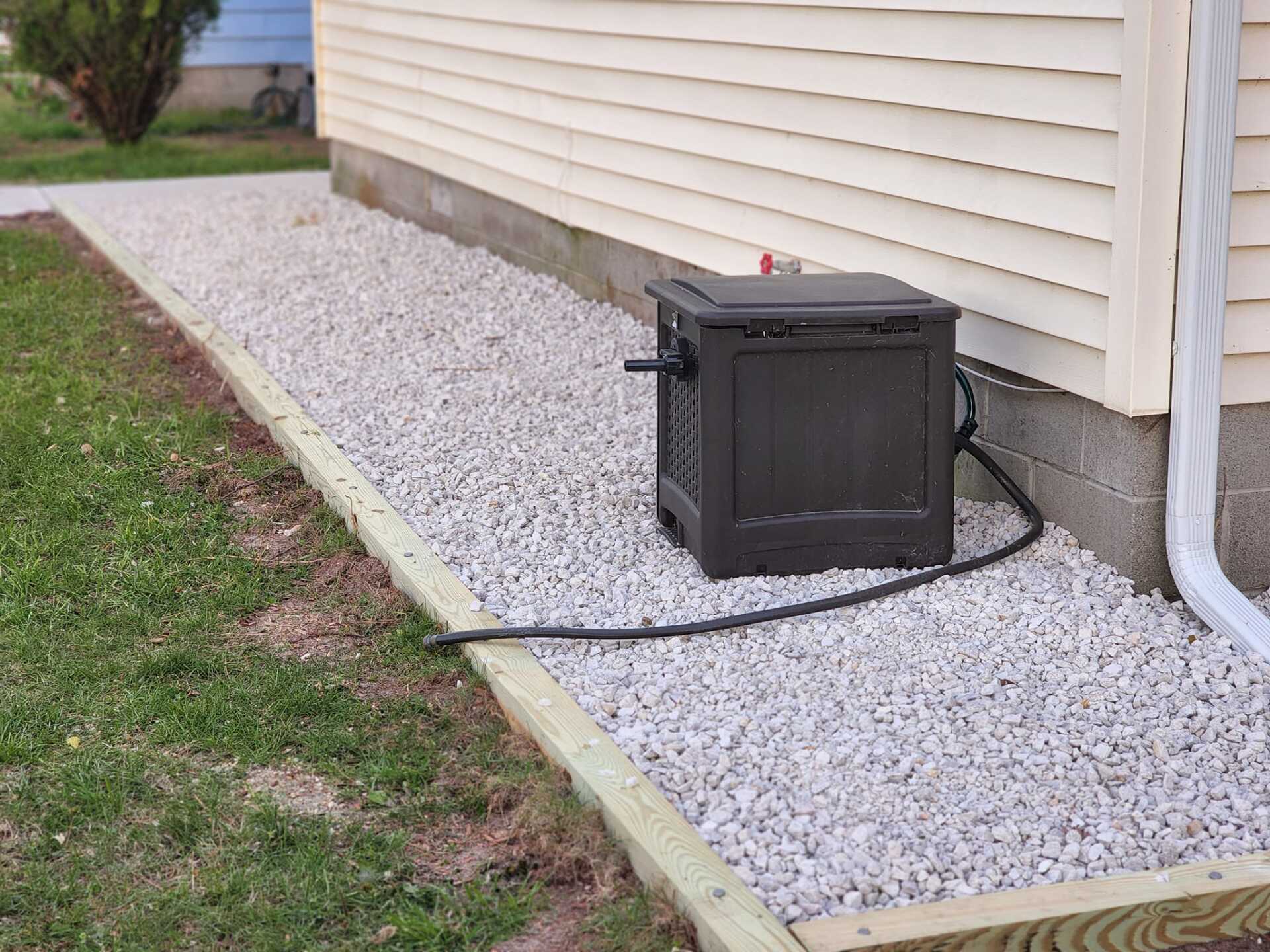A black box is sitting on a gravel sidewalk next to a house.