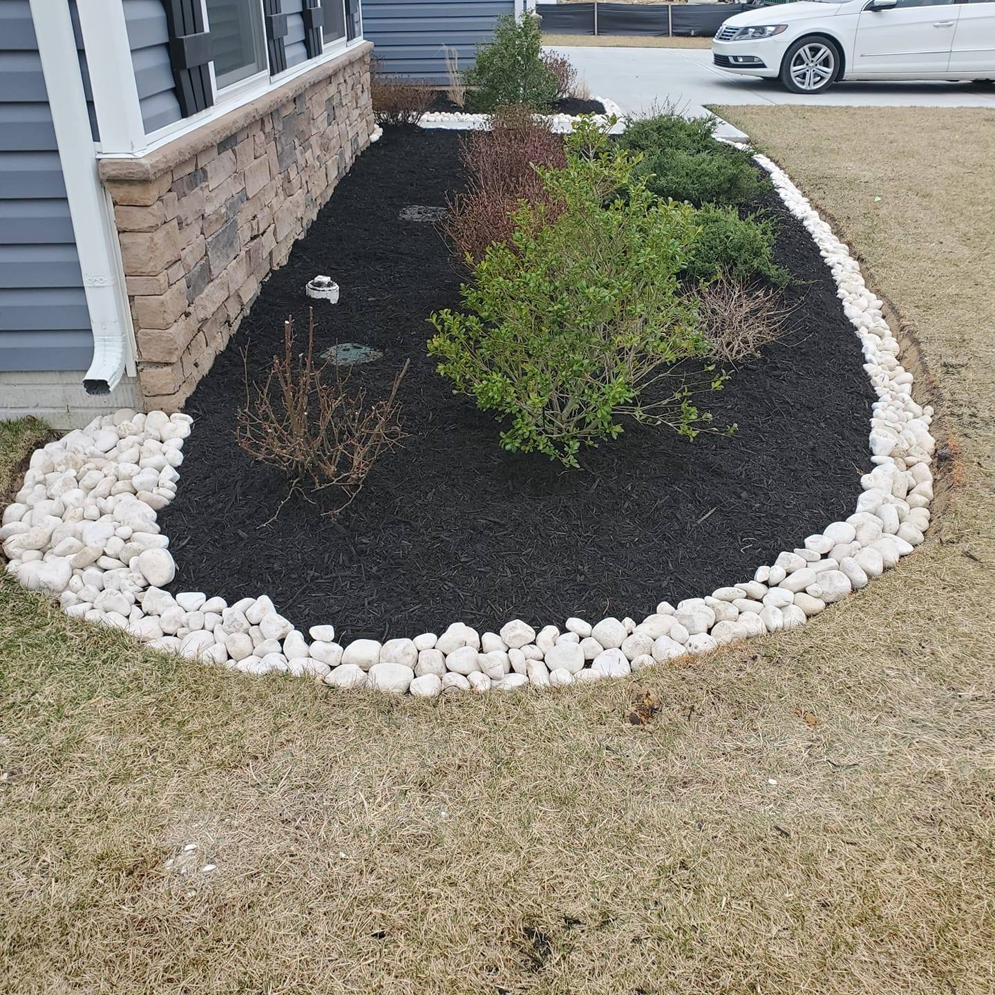 A white car is parked in a driveway next to a lush green garden.