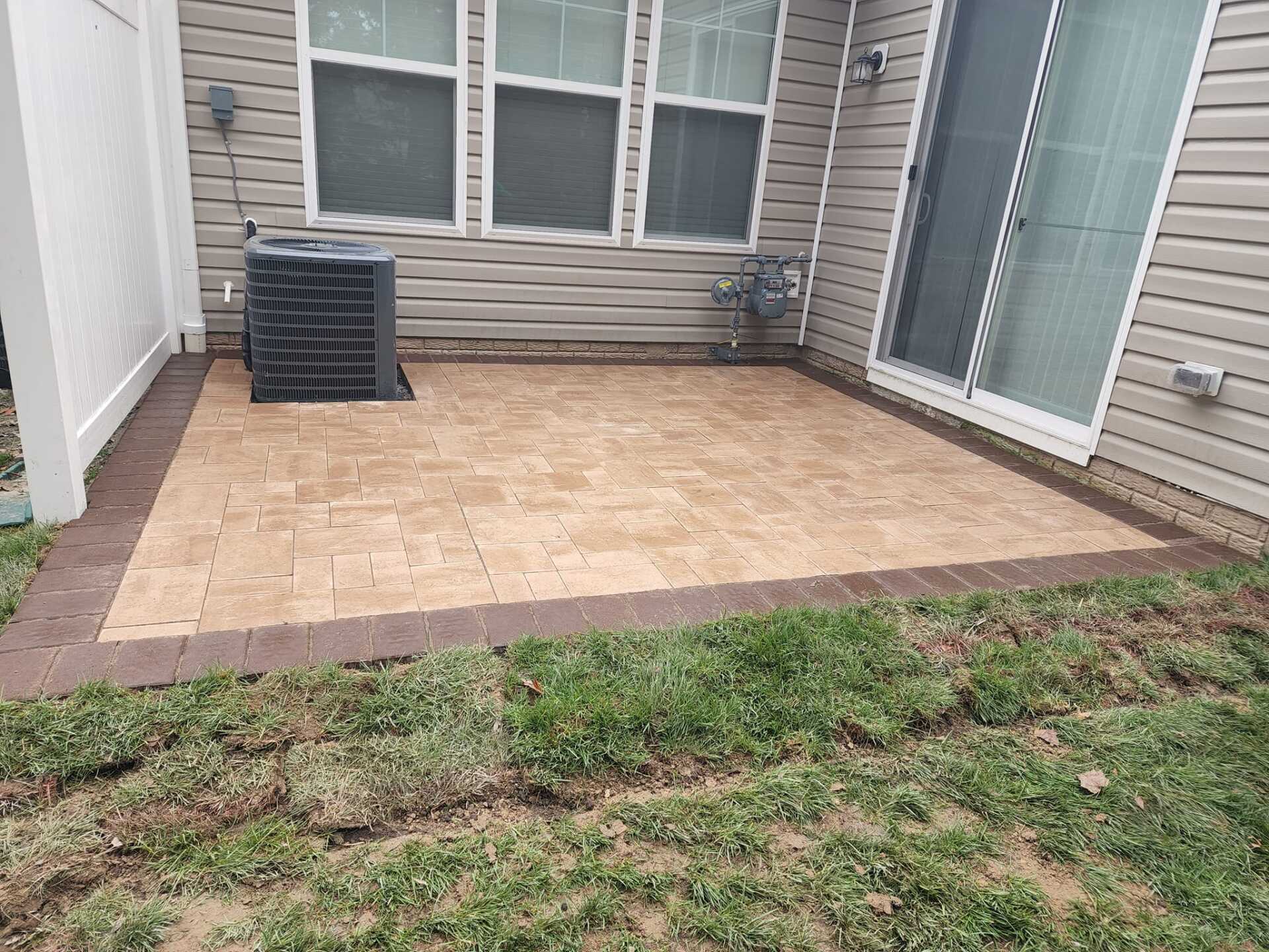 A patio with a sliding glass door in the backyard of a house.