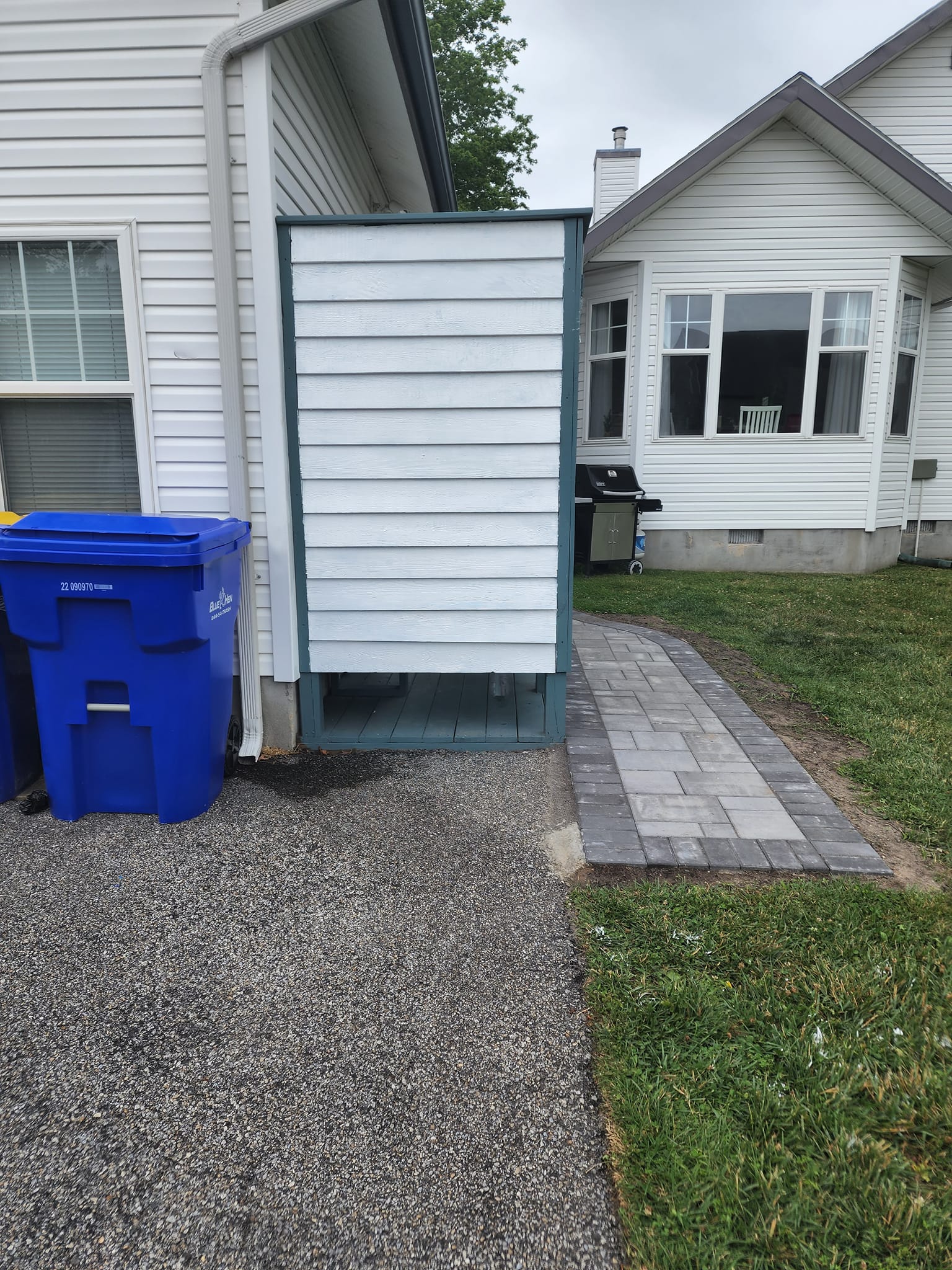 A blue trash can is sitting in front of a white house.