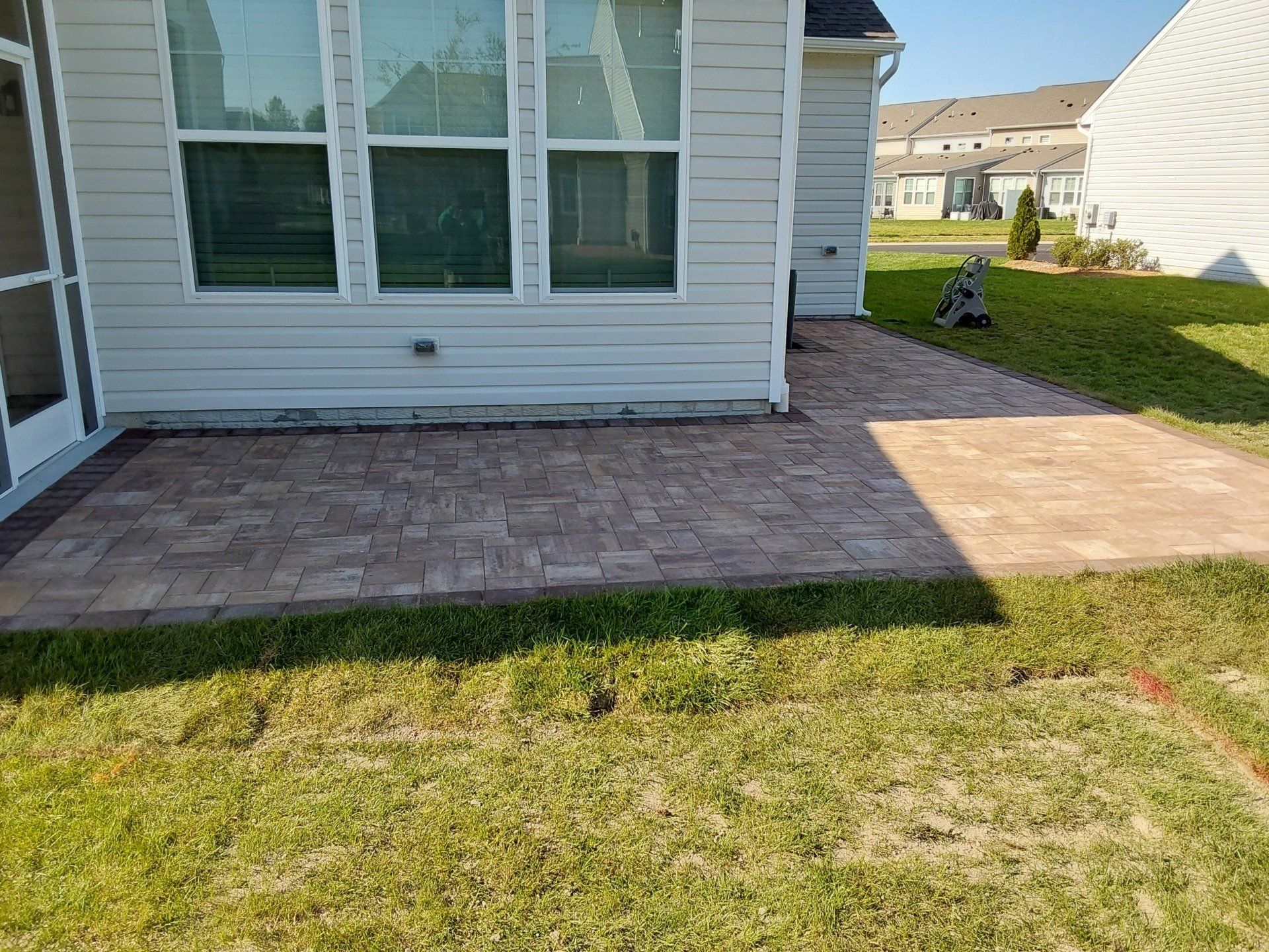 There is a patio in front of a house with a screened in porch.