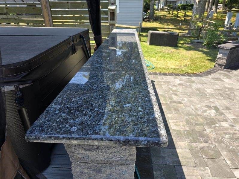 A granite counter top is sitting on a brick patio next to a hot tub.