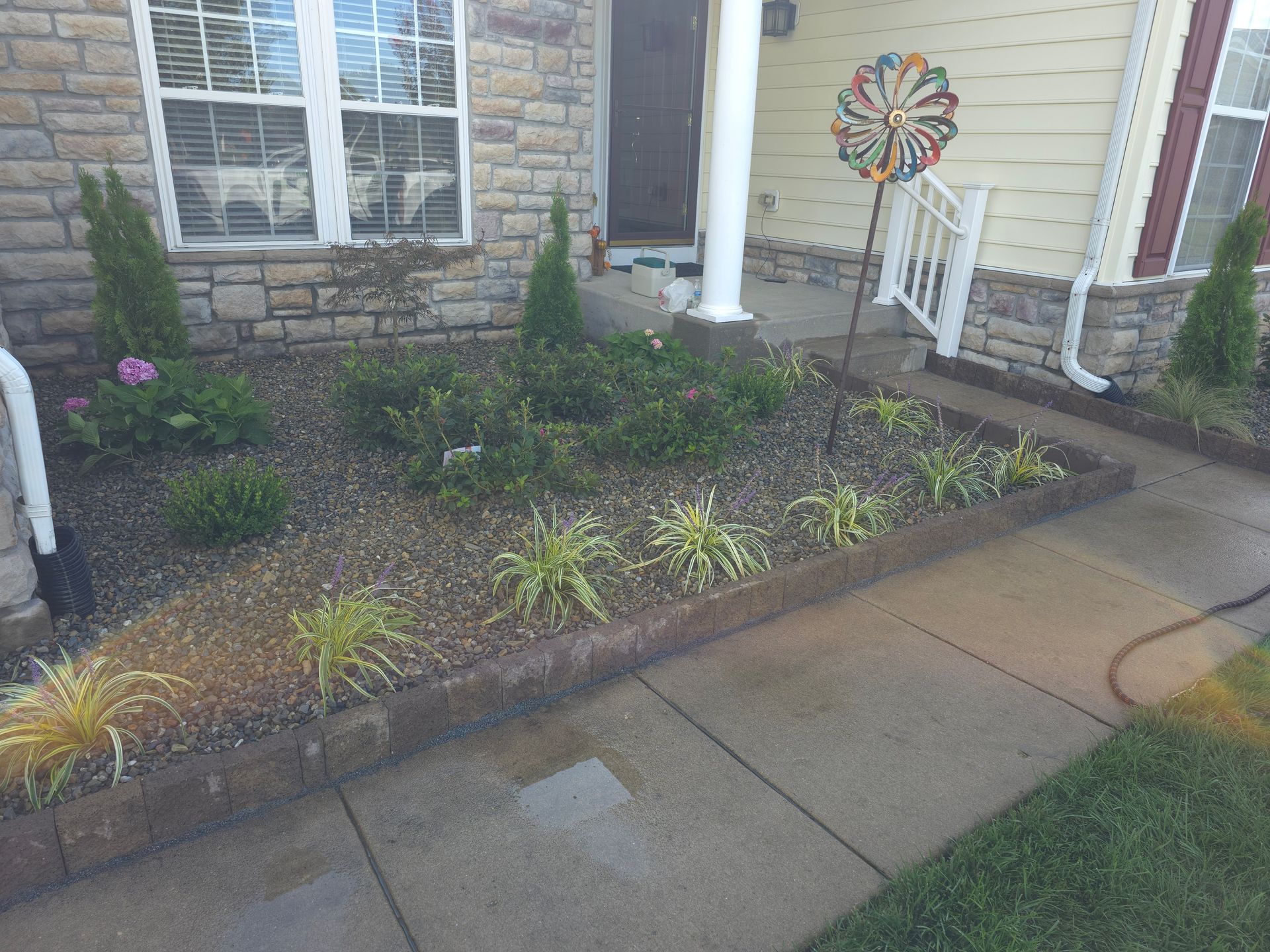 A concrete walkway leading to a house with a garden in front of it.