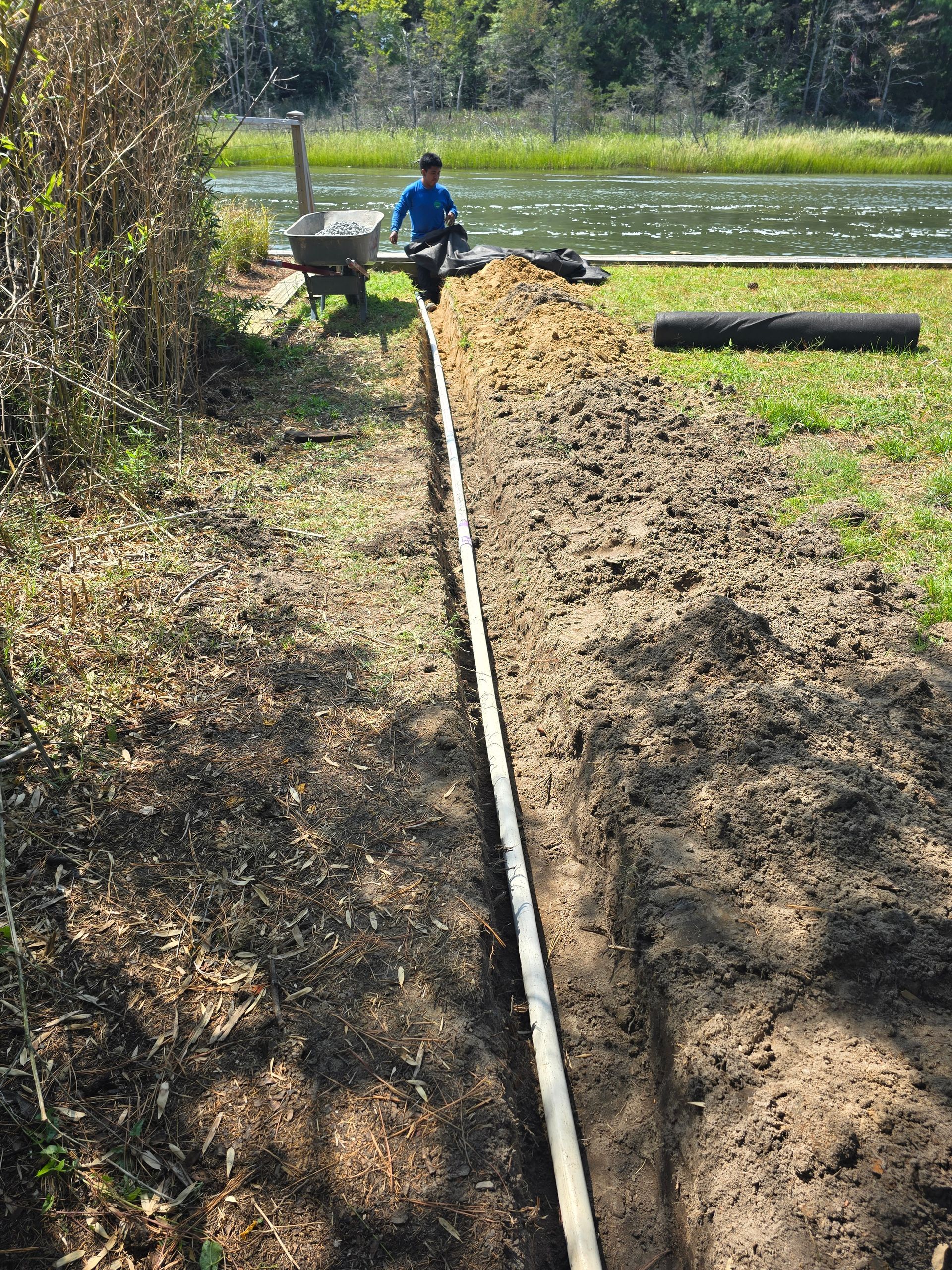 A man is sitting on top of a pile of dirt next to a river.