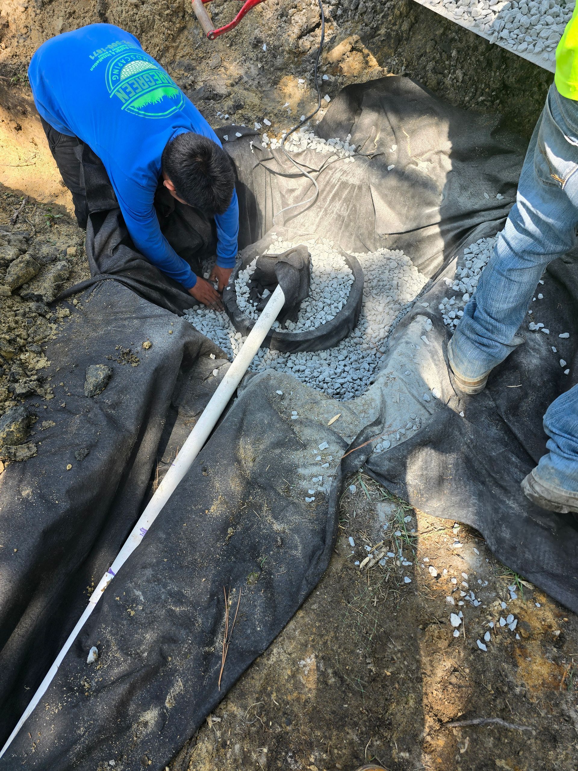 A man in a blue shirt is working on a pipe in the dirt.