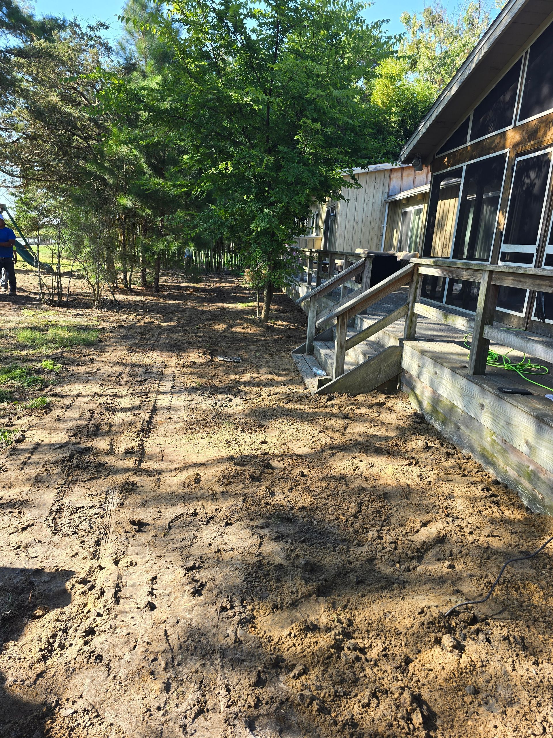 A dirt path leading to a house with stairs and trees in the background.