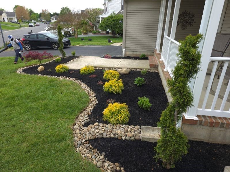 A man is standing in front of a house with a black car parked in the driveway.
