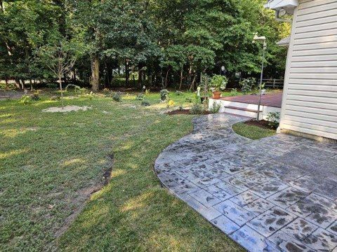 There is a concrete walkway leading to a house in the backyard.