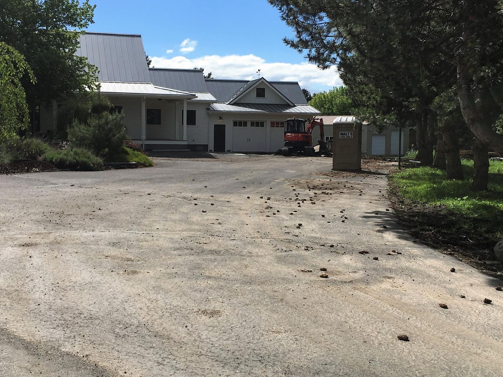 A gravel driveway leads to a light-colored house. A small excavator sits near the garage.