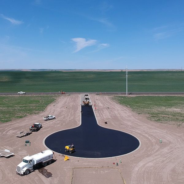 Road construction: Asphalt being laid for a roundabout in a rural setting under a blue sky.