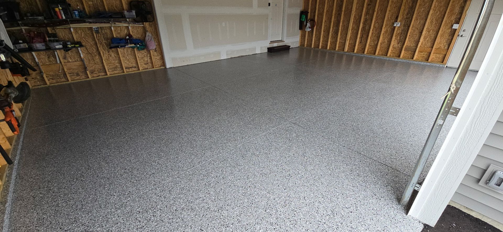 Garage with gray speckled epoxy floor. Wooden walls and open door.