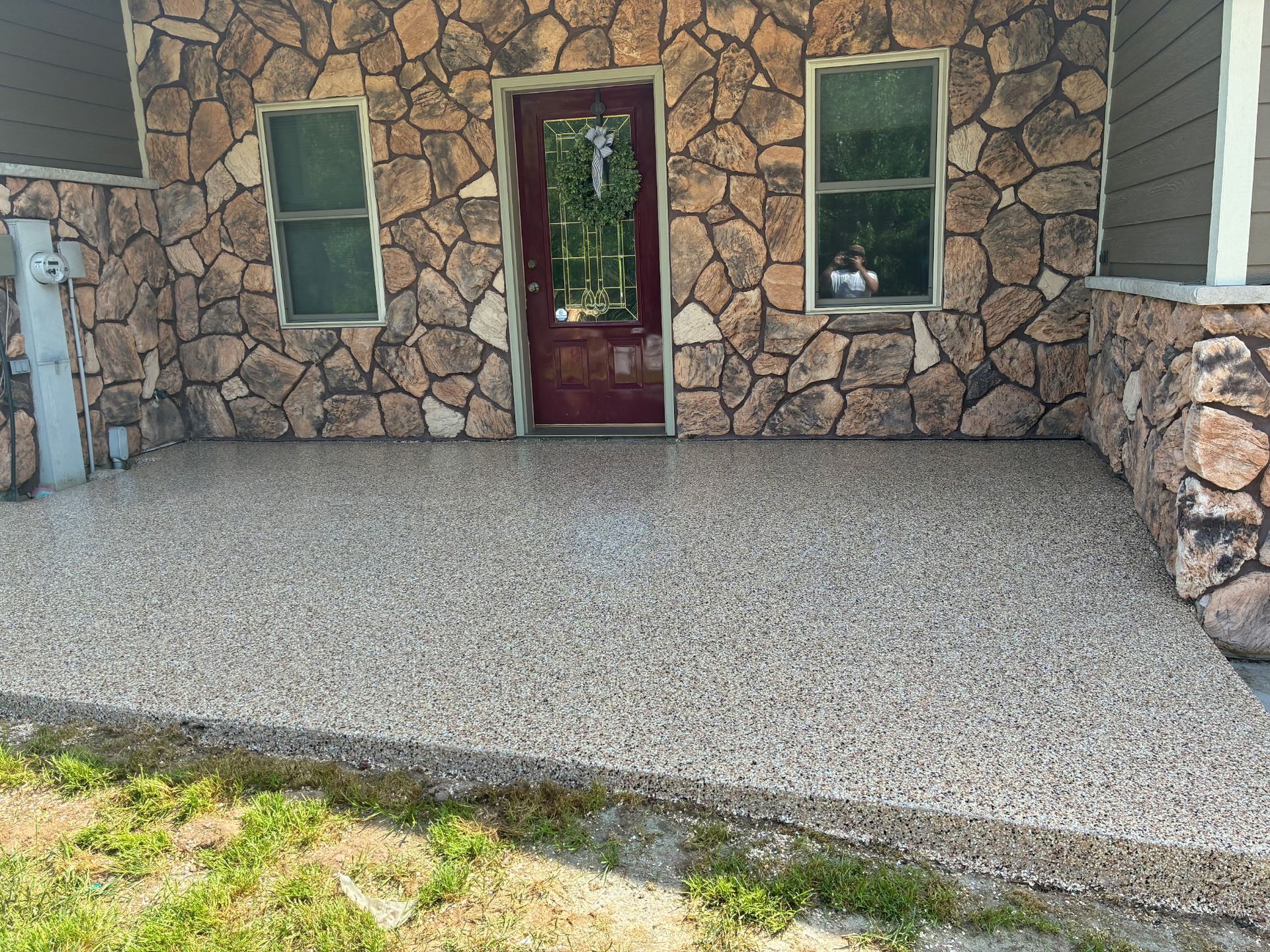 Porch with stone wall and floor, burgundy door, and two windows.