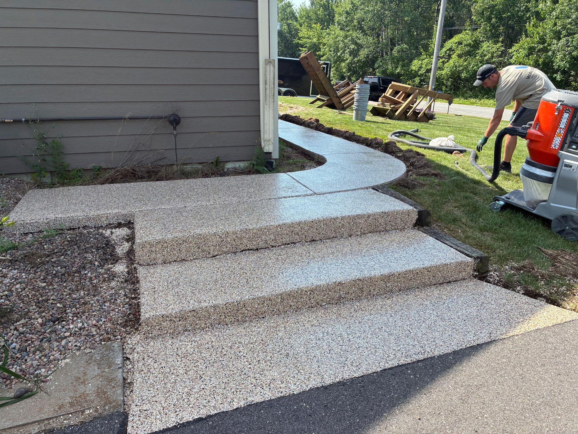 A newly constructed concrete walkway and steps. A worker uses a machine to finish the edges of the walkway.