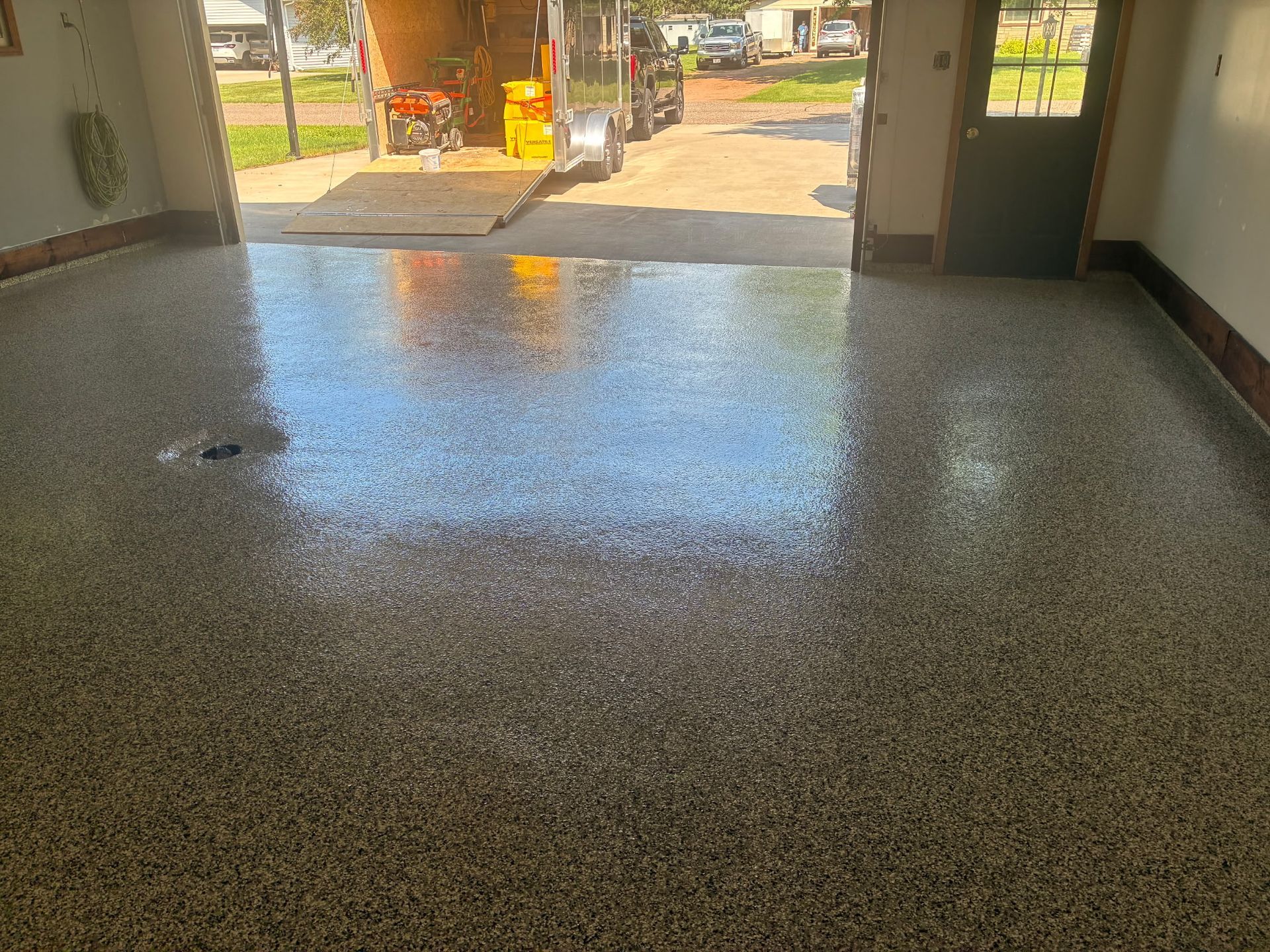 Shiny speckled epoxy garage floor. Open door, trailer and sunlight visible.