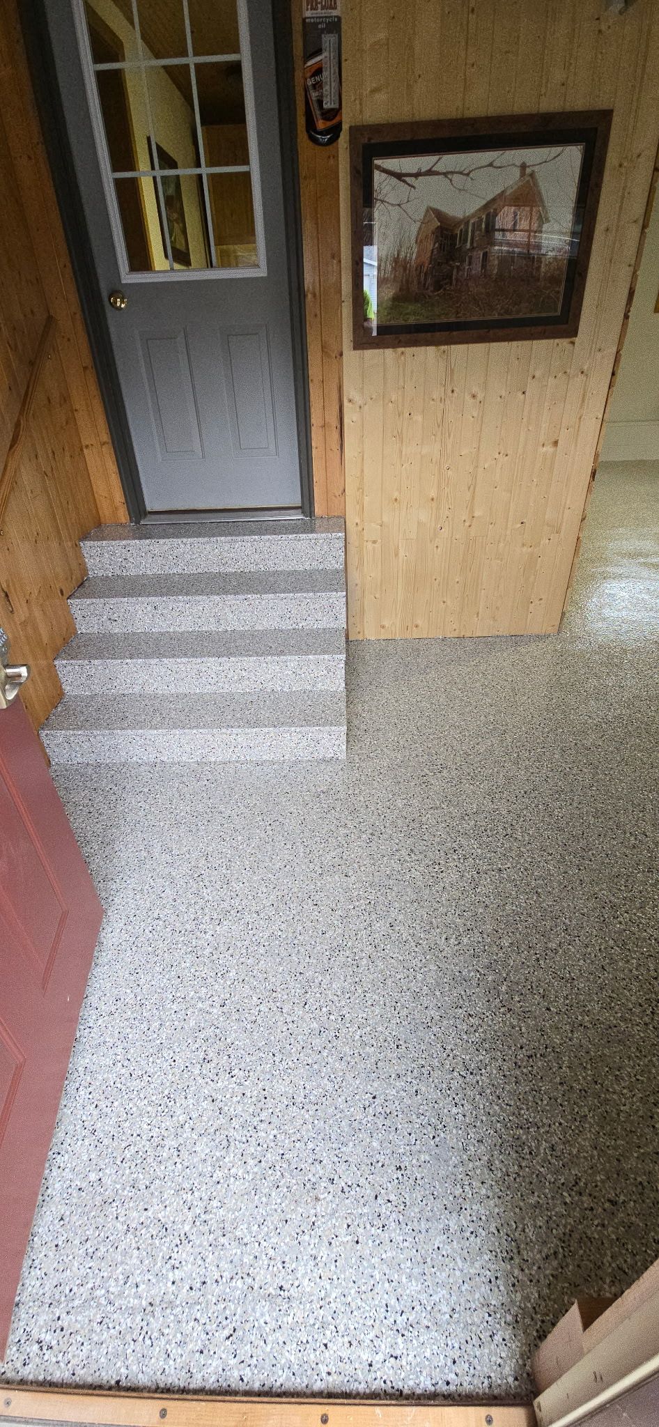 Entryway with steps leading to a gray door, gray pebble floor, and artwork on the wall.
