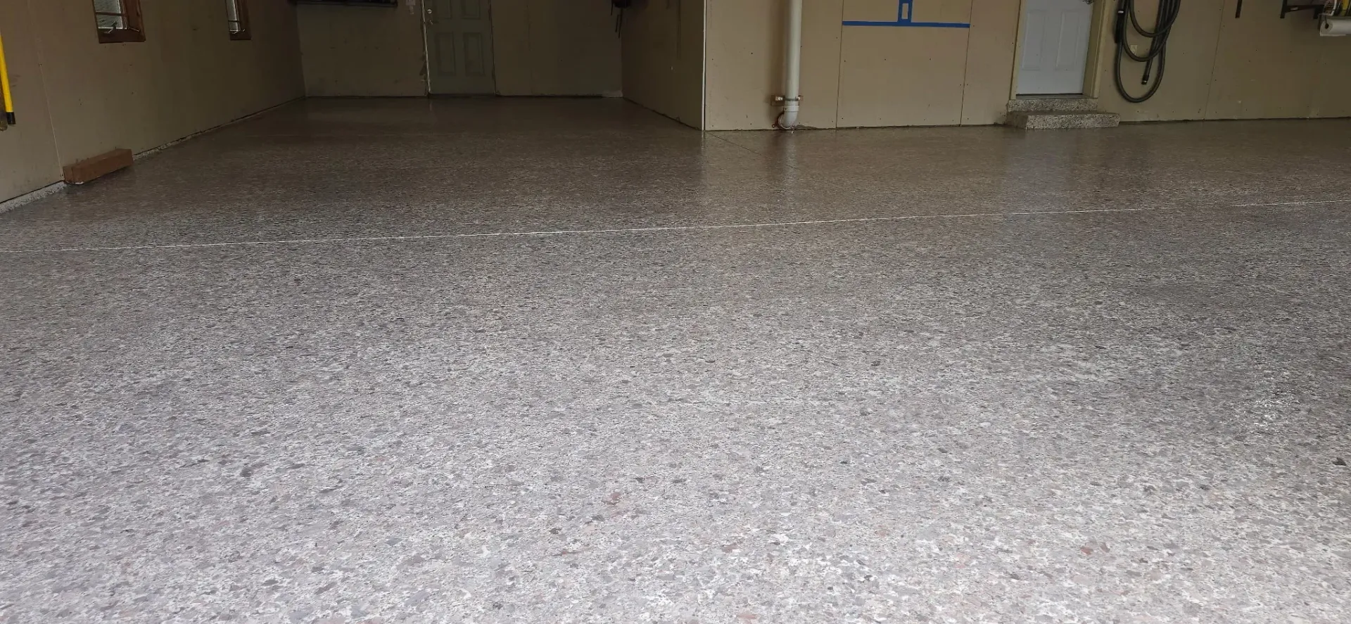 A room with a speckled floor, light-colored walls, and a door with graffiti.