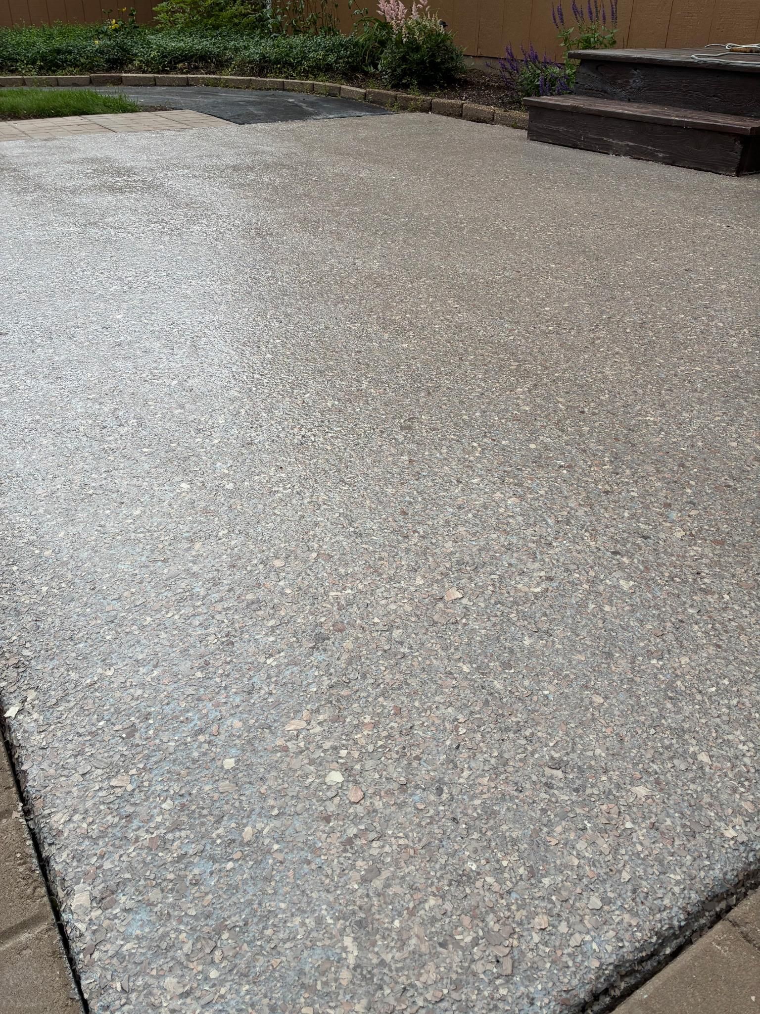 Gray aggregate patio with steps and greenery in the background.