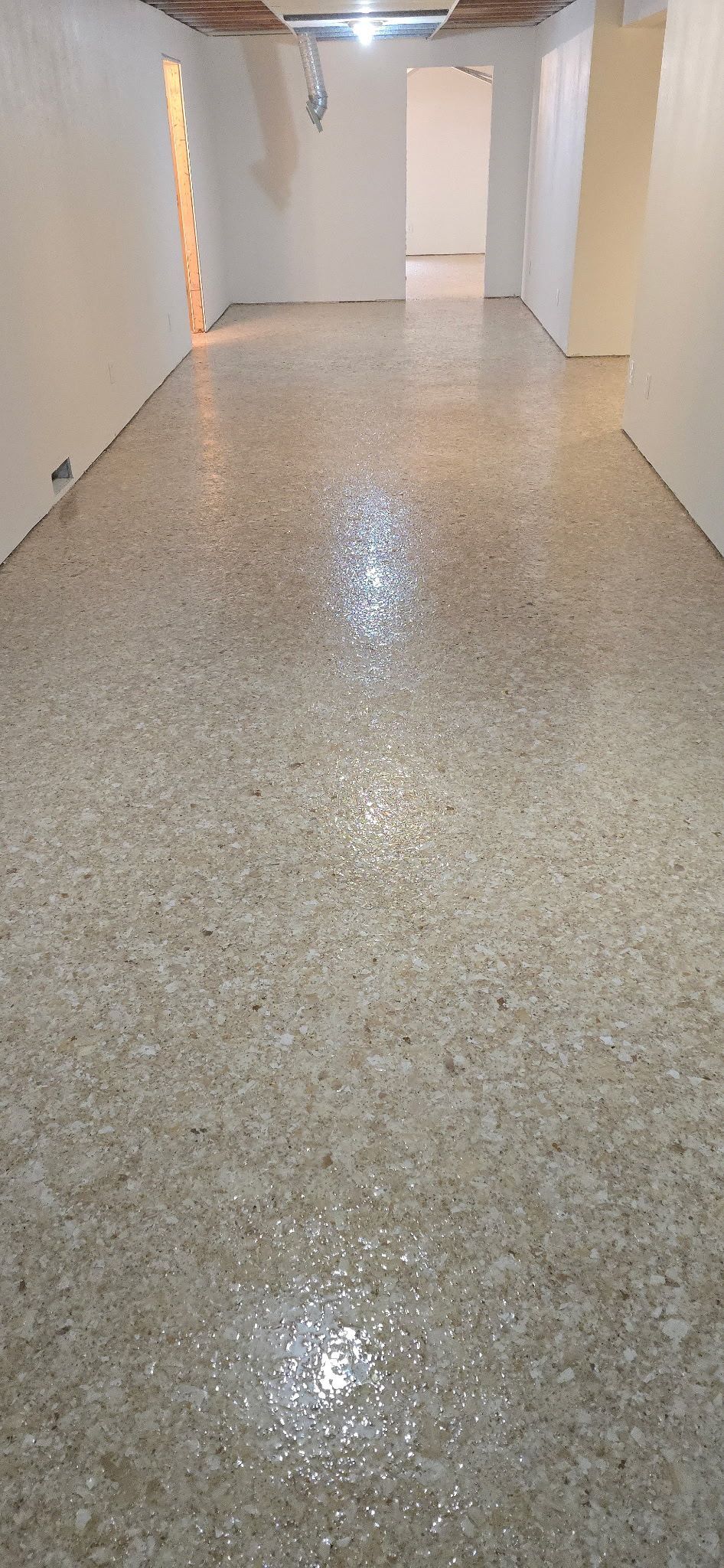 A narrow, well-lit hallway with a polished, speckled floor and white walls.