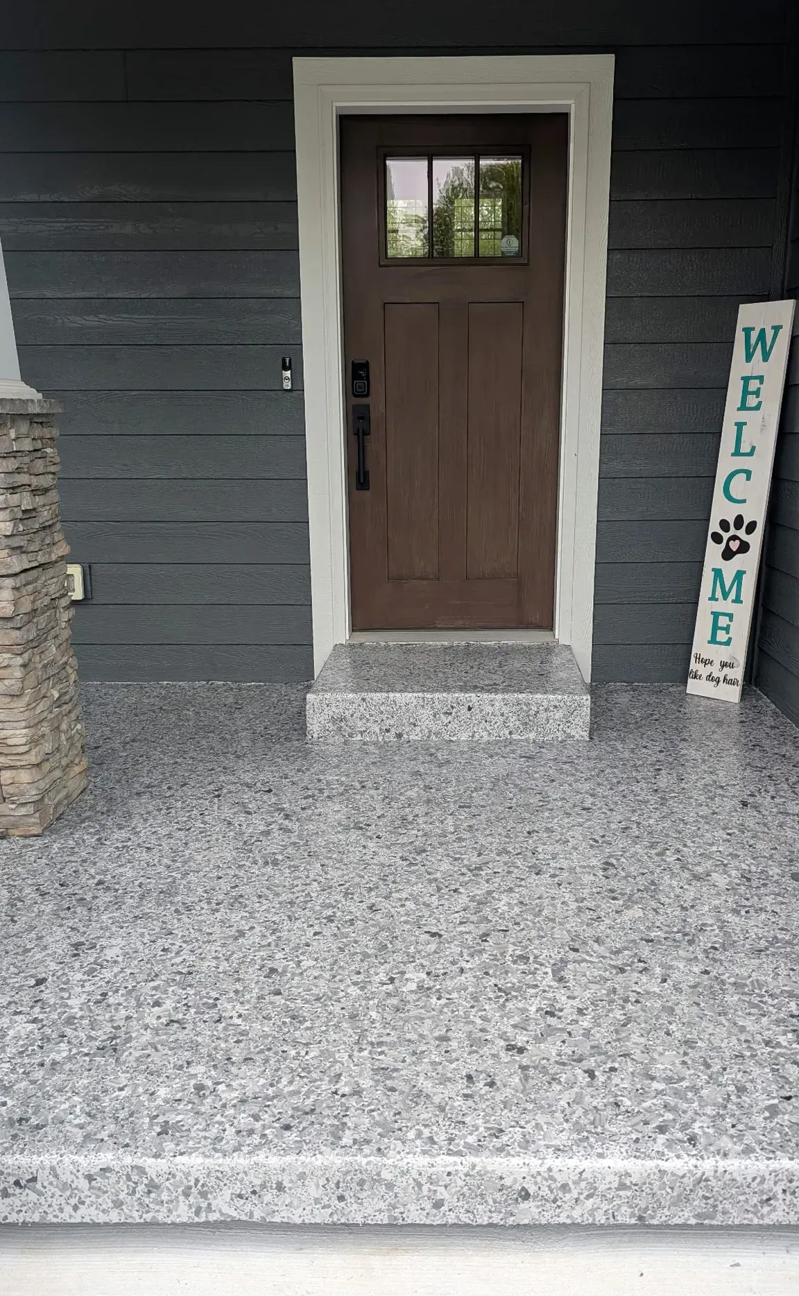 A brown front door with a welcome sign on a gray speckled porch.