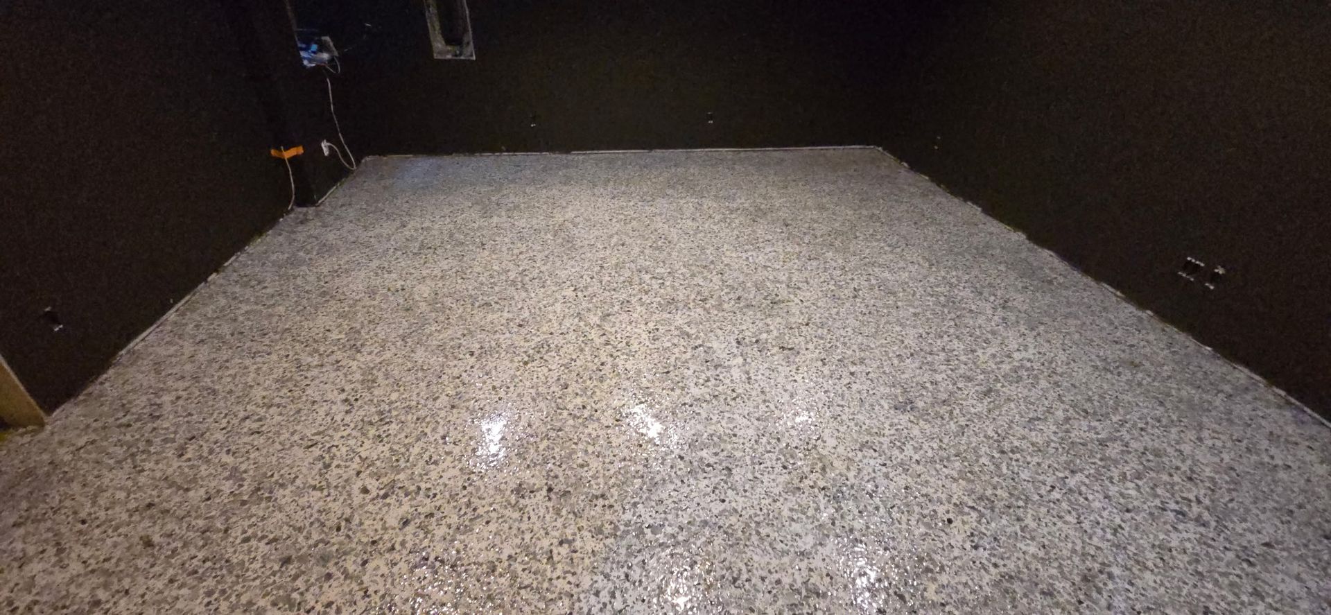 An indoor space with a gray, textured floor, surrounded by dark walls.