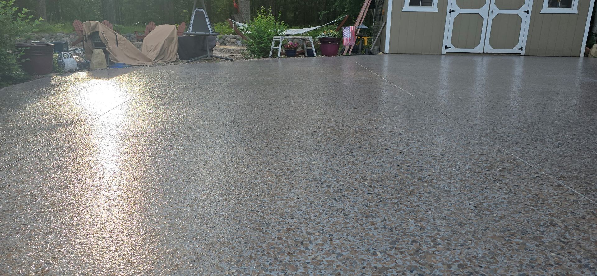 Gravel driveway with shed and foliage in the background, illuminated by sunlight.