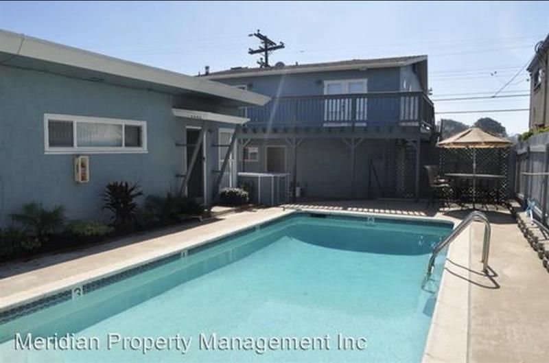 Swimming pool in backyard, two-story blue building, patio furniture, sunny day.