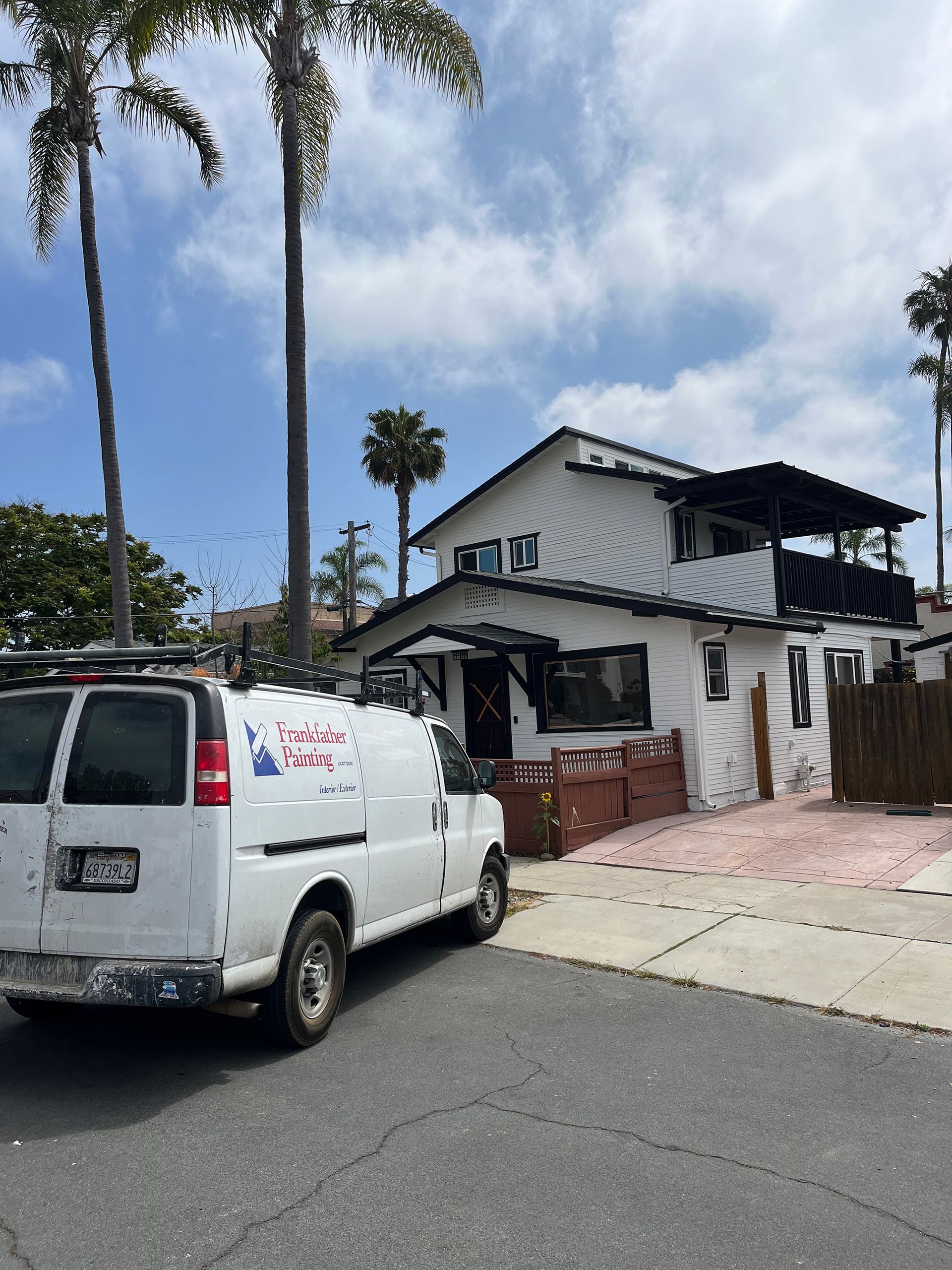 White house with black trim, a white van parked in front, palm trees, sunny day.