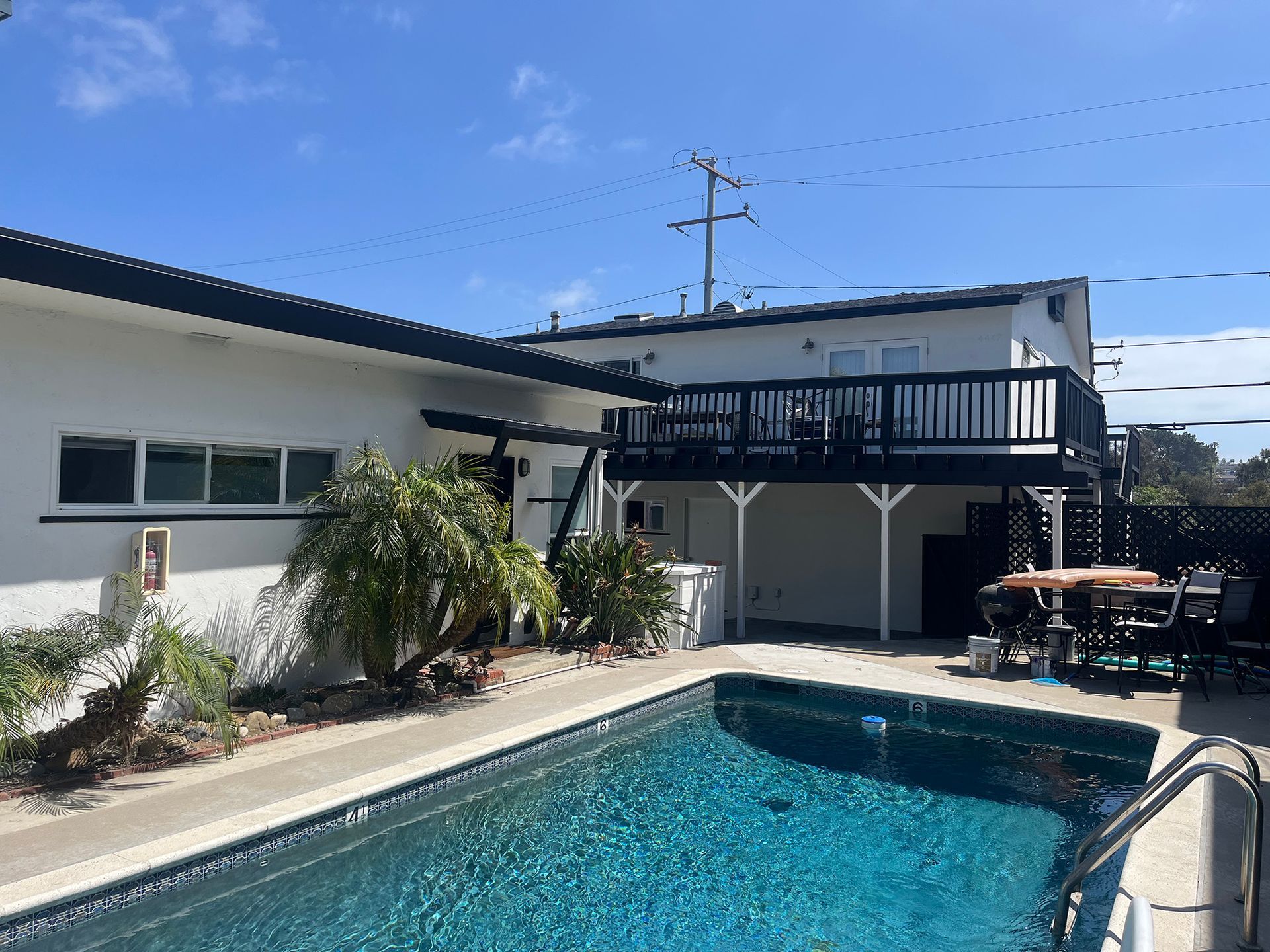 Backyard with pool, deck, and white house under a blue sky.