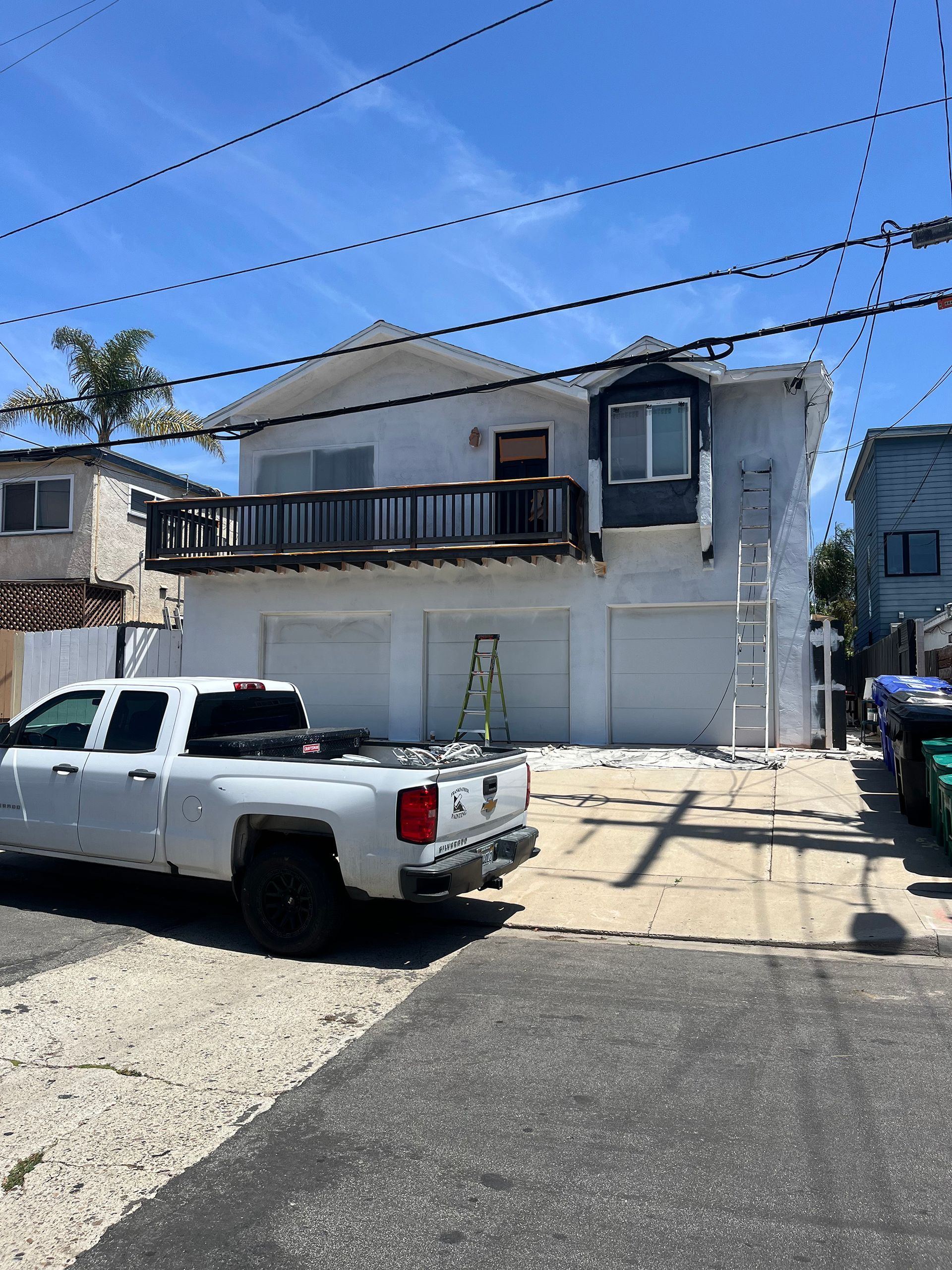 White two-story house with deck and garage, white truck parked in front. Blue sky overhead.