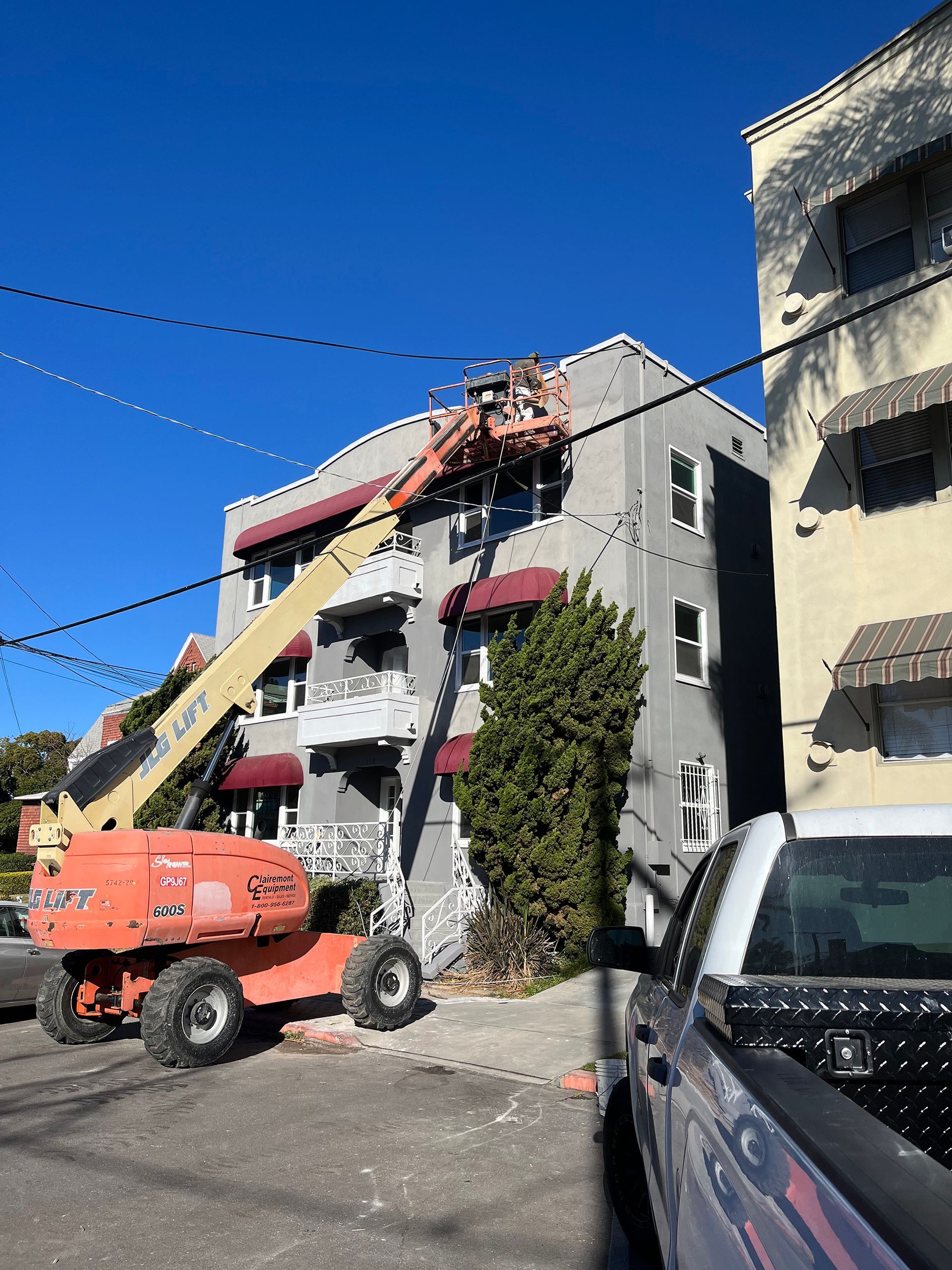 Orange lift truck next to a gray apartment building with workers.