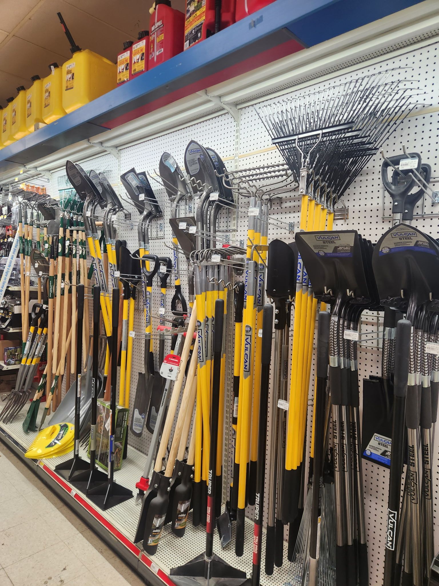 A bunch of shovels and brooms are hanging on a wall in a store.