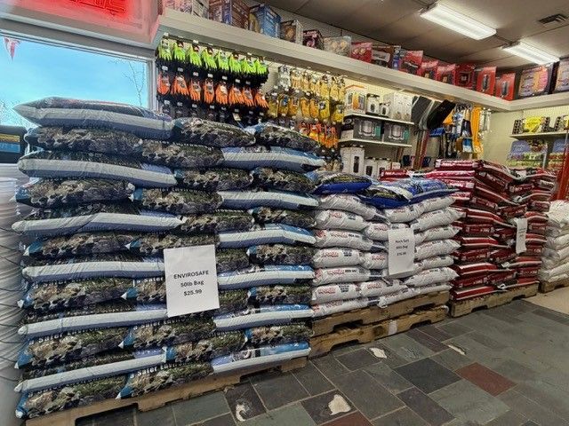 Shelves of animal feed bags in a store. Several pallets hold stacks of different colored bags.