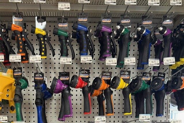 Hose nozzles on display, various colors and styles, hanging on a retail shelf with price tags.