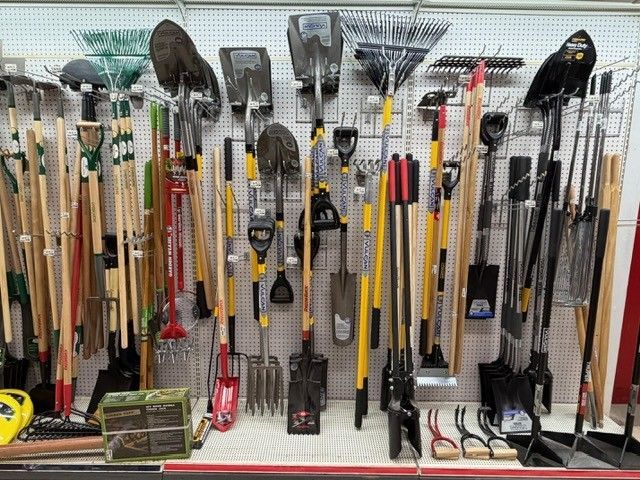 Garden tools displayed on a pegboard wall: shovels, rakes, hoes, and hand tools.