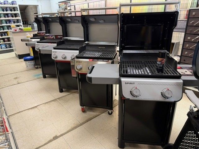 Row of new gas grills on display in a store, black and silver.
