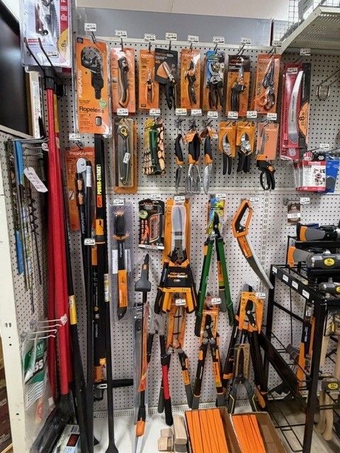 Tools display: orange and black hand tools, saws, and measuring equipment on a pegboard wall in a store.