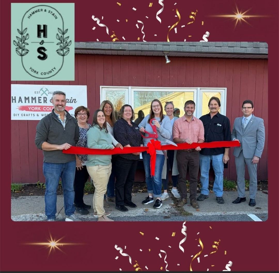 People cut a red ribbon in front of a building with a business sign.